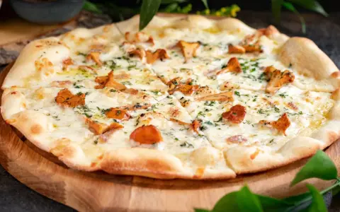 Pyszna pizza z kurkami, roztopionym serem i ziołami, podana na drewnianej desce.