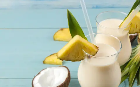 Dwa orzeźwiające koktajle pina colada z kawałkami ananasa i kokosem na niebieskim tle.