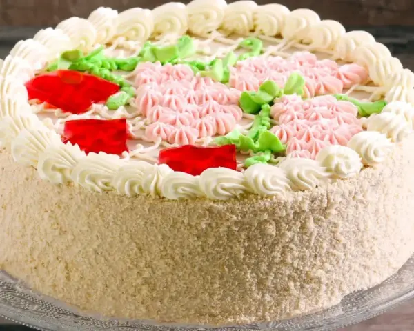Elegancki tort udekorowany kremem, różowymi kwiatkami, zielonymi listkami i czerwonymi galaretkami. Pyszny krem do tortu zachwyca smakiem.