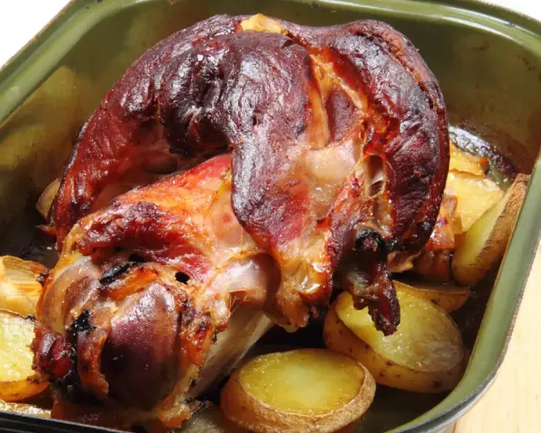 Zapieczona golonka z ziemniakami w naczyniu. Idealny sposób, jak zapeklować golonkę, by była soczysta i aromatyczna.