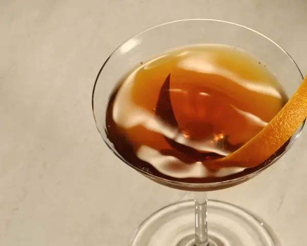 Elegancki Rob Roy cocktail w kieliszku, ozdobiony skórką pomarańczy.