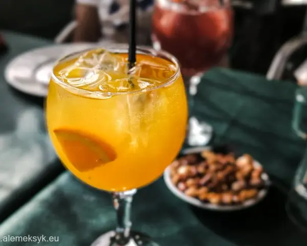 Orzeźwiający drink agua de valencia z plasterkiem pomarańczy i lodem, na stole obok miseczki z orzeszkami.