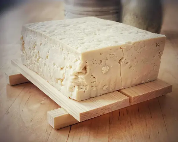 Kostka białego tofu, zrobionego z soi, na drewnianej podstawce.