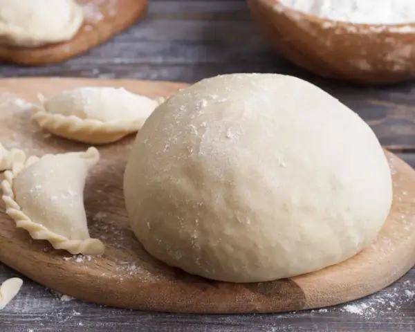 Gotowe ciasto na pierogi i kilka uformowanych pierożków na desce. Czy ciasto na pierogi można zrobić dzień wcześniej? Tak, można!