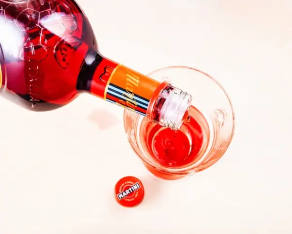 Czerwony Martini Fiero drink nalewany z butelki do szklanki. Obok leży czerwona zakrętka z logo Martini.