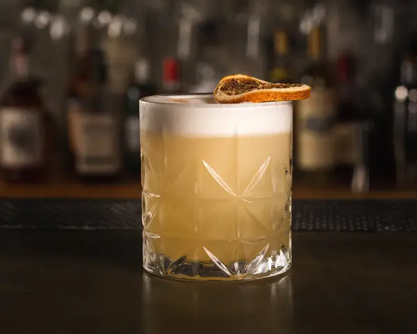Idealny drink whisky sour z pianką i plasterkiem suszonej pomarańczy, gotowy do degustacji.