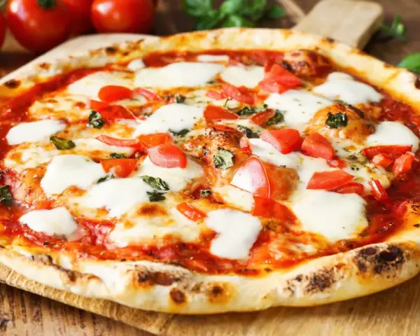 Pyszne ciasto na pizzę bez wyrastania, z pomidorami, mozzarellą i bazylią, na drewnianej desce.