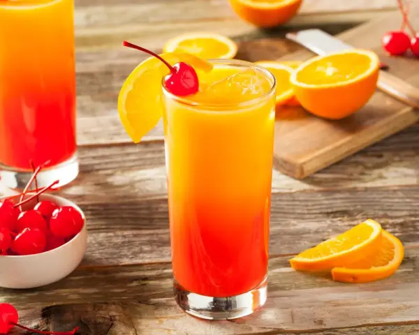 Dwa drinki z grenadyną, ozdobione plasterkami pomarańczy i wiśniami, stoją na drewnianym stole.