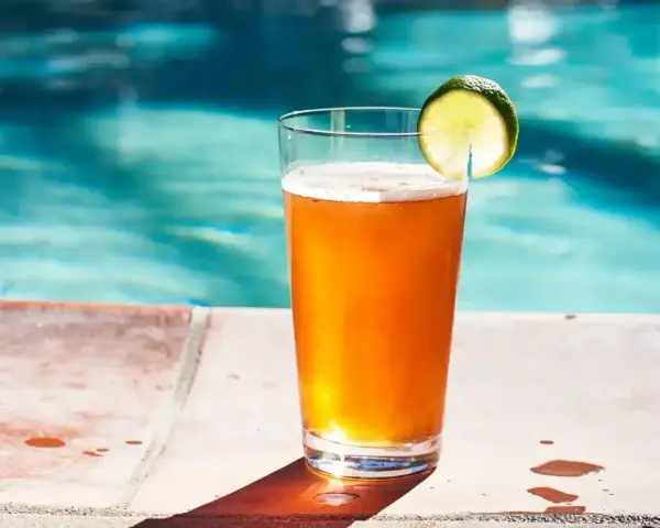 Orzeźwiający drink z piwem i plasterkiem limonki, stojący na brzegu basenu. Idealny na upalne dni.