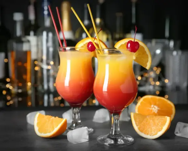 Dwa drinki z wódką, udekorowane pomarańczą i wiśnią, z kostkami lodu i owocami na blacie. Idealne domowe drinki z wódką na letnie wieczory.