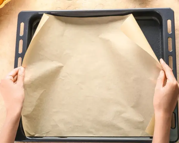 Ręce układają papier do pieczenia na blasze. Zastanawiasz się, czym zastąpić papier do pieczenia? Oto praktyczne rozwiązanie!