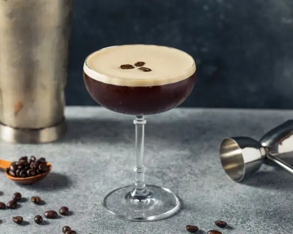 Elegancki drink z kawą, ozdobiony ziarnami kawy, obok shakera i miarki barmańskiej. Idealny na pobudzenie.
