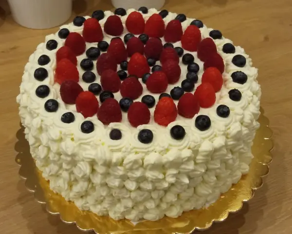Pyszny tort bezglutenowy ozdobiony bitą śmietaną, malinami i borówkami. Idealny na każdą okazję, a przepis na niego jest prosty!