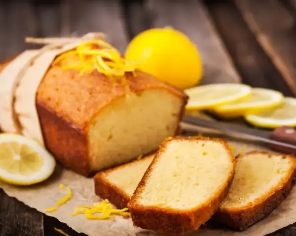 Wilgotna babka piaskowa z cytryną, ozdobiona skórką, podana z plasterkami cytryny.