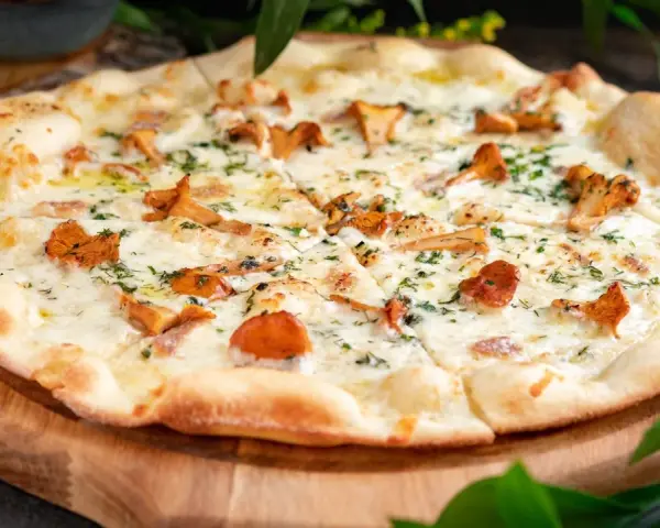 Pyszna pizza z kurkami, roztopionym serem i ziołami, podana na drewnianej desce.