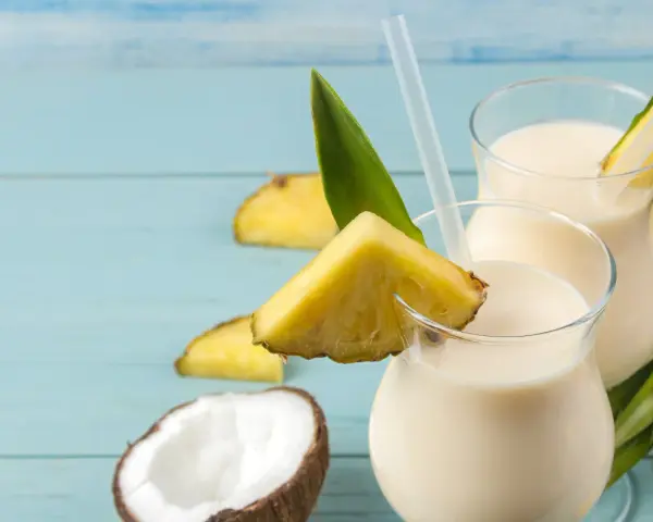 Dwa orzeźwiające koktajle pina colada z kawałkami ananasa i kokosem na niebieskim tle.