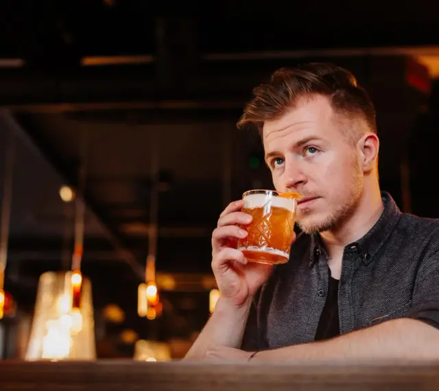 Mężczyzna sączy orzeźwiający whisky sour, delektując się smakiem w nastrojowym barze.