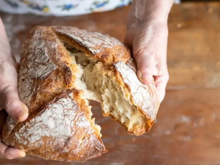 Ręce rozrywają świeży, chrupiący bochenek. Zastanawiasz się, jakie mąki na chleb bezglutenowy wybrać, by uzyskać taki efekt?