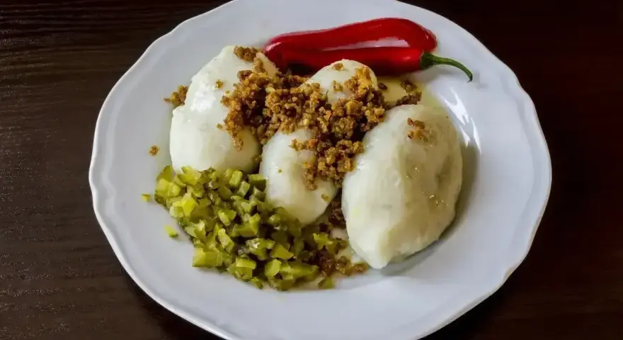 Trzy sycące kartacze z mięsem, posypane skwarkami, z dodatkiem ogórka kiszonego i ostrej papryczki.