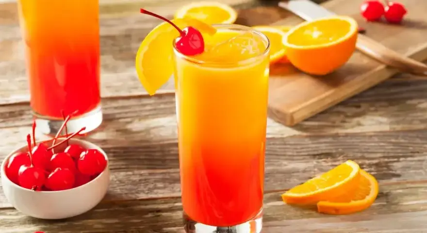 Kolorowy drink tequila sunrise z pomarańczą i wiśnią, idealny na letnie wieczory.