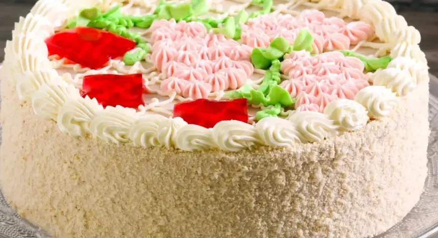 Elegancki tort udekorowany kremem, różowymi kwiatkami, zielonymi listkami i czerwonymi galaretkami. Pyszny krem do tortu zachwyca smakiem.