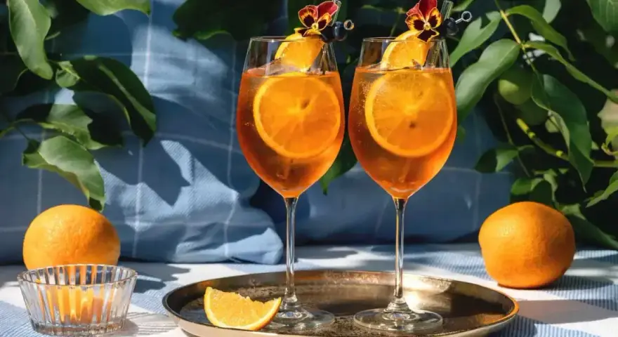 Dwa orzeźwiające drinki z aperolem i sokiem pomarańczowym, ozdobione plastrami pomarańczy i kwiatami, gotowe na letnie popołudnie.