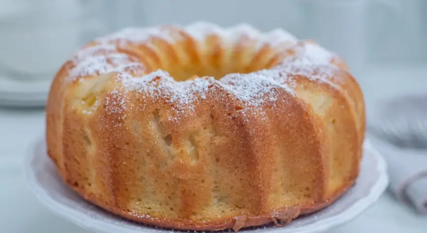 Najlepsza babka cytrynowa wilgotna na oleju, oprószona cukrem pudrem, prezentuje się apetycznie na białej paterze.