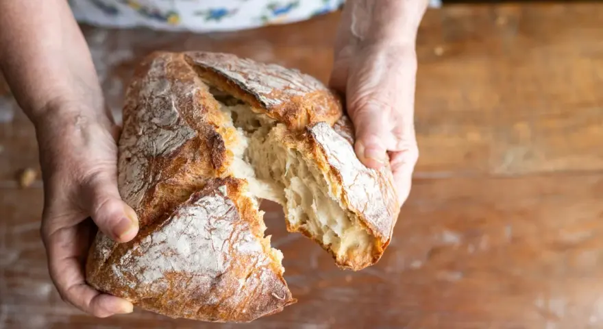 Ręce rozrywają świeży, chrupiący bochenek. Zastanawiasz się, jakie mąki na chleb bezglutenowy wybrać, by uzyskać taki efekt?