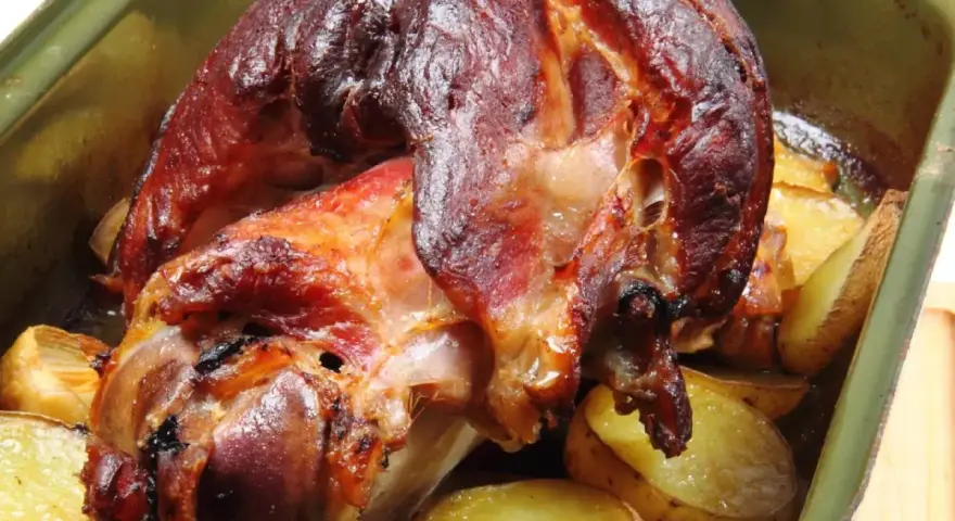 Zapieczona golonka z ziemniakami w naczyniu. Idealny sposób, jak zapeklować golonkę, by była soczysta i aromatyczna.