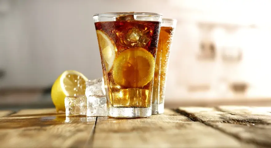 Dwa orzeźwiające drinki Long Island Iced Tea z plasterkami cytryny i lodem na drewnianym blacie.