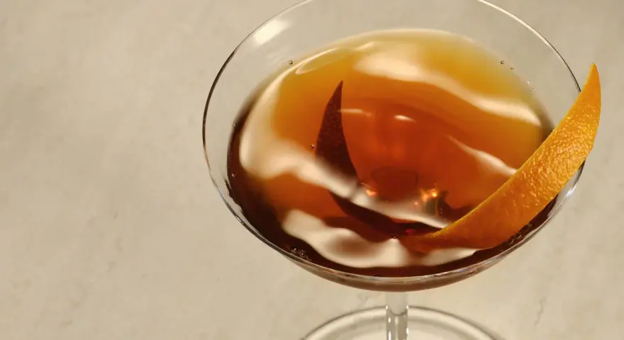 Elegancki Rob Roy cocktail w kieliszku, ozdobiony skórką pomarańczy.