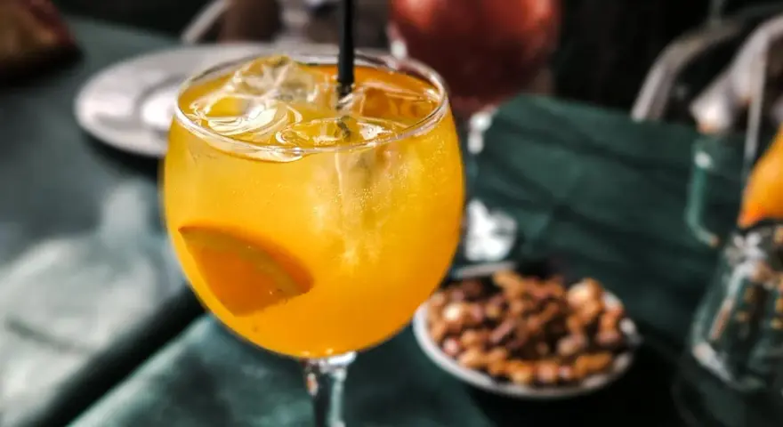 Orzeźwiający drink agua de valencia z plasterkiem pomarańczy i lodem, na stole obok miseczki z orzeszkami.
