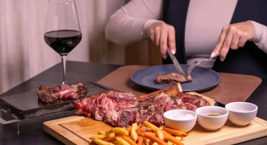 Idealne wino do dziczyzny? Czerwone, pełne, jak to w kieliszku obok soczystego steka i frytek. Ktoś kroi kolejny kawałek.