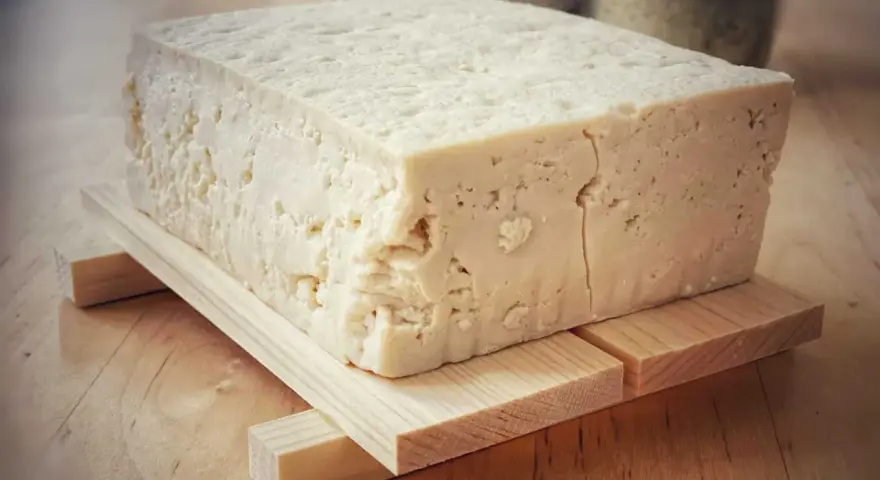 Kostka białego tofu, zrobionego z soi, na drewnianej podstawce.