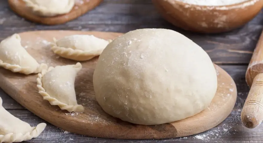 Gotowe ciasto na pierogi i kilka uformowanych pierożków na desce. Czy ciasto na pierogi można zrobić dzień wcześniej? Tak, można!