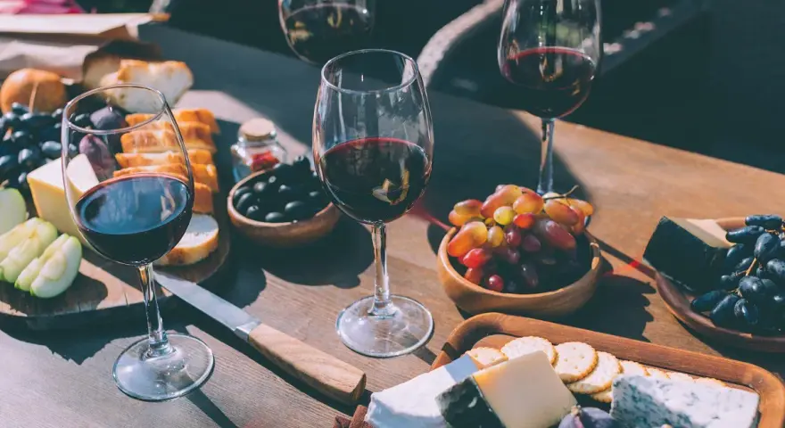 Degustacja wina merlot: jakie to wino? Kieliszki pełne rubinowego trunku, deska serów, winogrona, oliwki i figi tworzą idealną kompozycję.