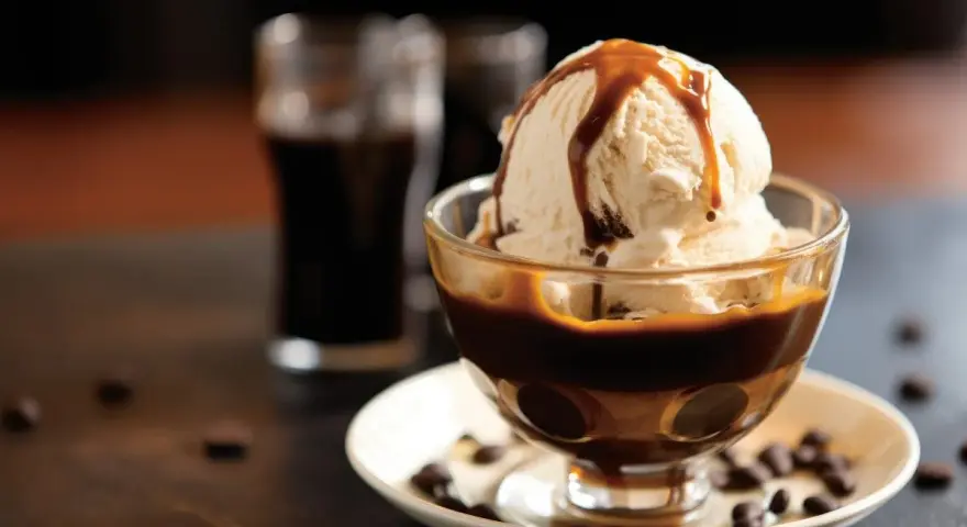 Lody waniliowe z syropem karmelowym w pucharku, obok szklaneczki z ciemnym napojem. Idealne połączenie, gdy zastanawiasz się, **Baileys z czym pić**.
