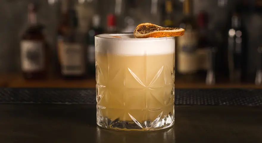 Idealny drink whisky sour z pianką i plasterkiem suszonej pomarańczy, gotowy do degustacji.