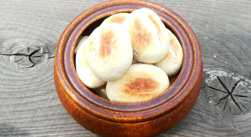 Małe, okrągłe bułki z ciasta na pizzę, lekko zarumienione, w brązowej misce na drewnianym stole.
