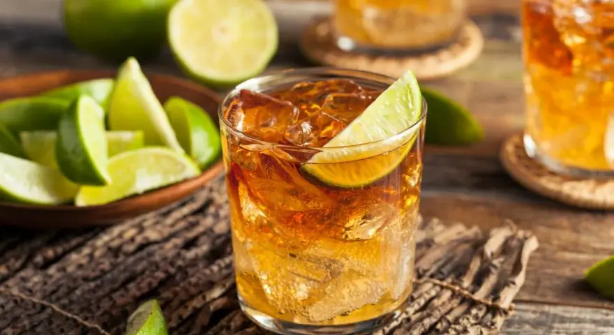 Idealny drink z rumem i lodem, ozdobiony plasterkiem limonki. Obok miseczka z kawałkami limonki, sugerująca, z czym pić rum.