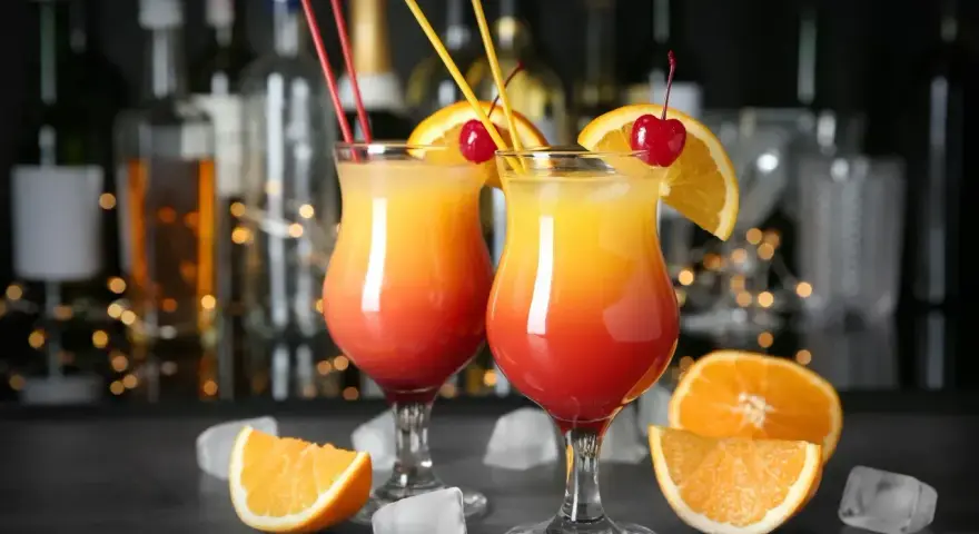 Dwa drinki z wódką, udekorowane pomarańczą i wiśnią, z kostkami lodu i owocami na blacie. Idealne domowe drinki z wódką na letnie wieczory.