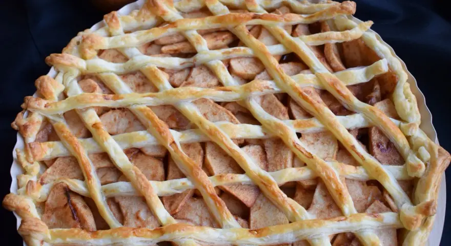 Pyszna tarta z ciasta francuskiego na słodko, wypełniona jabłkami i cynamonem, z kratką z ciasta na wierzchu.