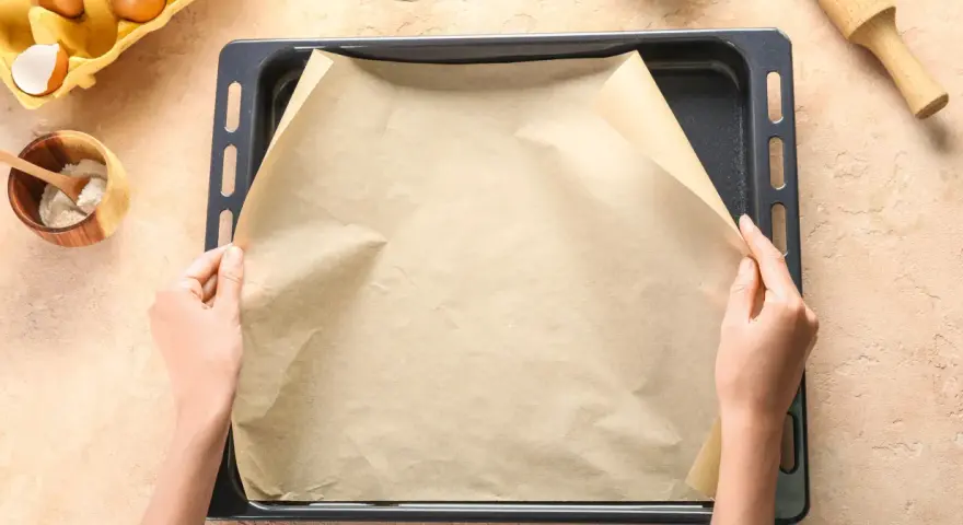 Ręce układają papier do pieczenia na blasze. Zastanawiasz się, czym zastąpić papier do pieczenia? Oto praktyczne rozwiązanie!