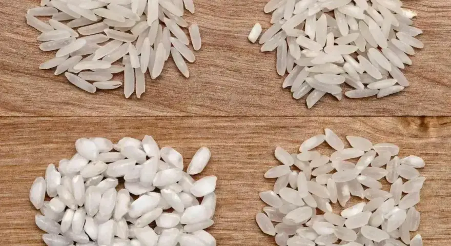 Cztery rodzaje ryżu, w tym ryż do risotto, ułożone na drewnianym tle.