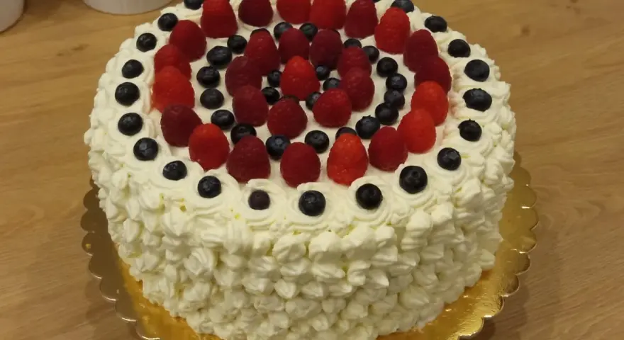 Pyszny tort bezglutenowy ozdobiony bitą śmietaną, malinami i borówkami. Idealny na każdą okazję, a przepis na niego jest prosty!
