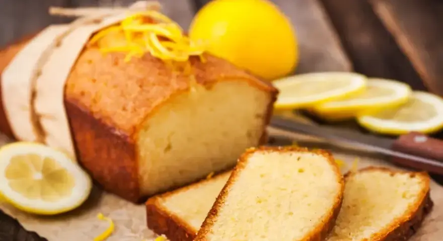 Wilgotna babka piaskowa z cytryną, ozdobiona skórką, podana z plasterkami cytryny.