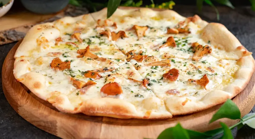 Pyszna pizza z kurkami, roztopionym serem i ziołami, podana na drewnianej desce.