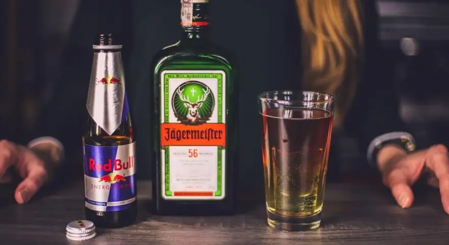 Butelka Jägermeister, puszka Red Bull i szklanka z drinkiem. Jägermeister to niemiecki likier ziołowy, często mieszany z napojami energetycznymi.