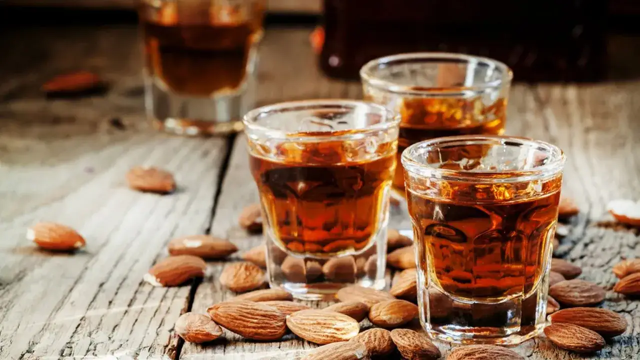 Amaretto co to? Bursztynowy likier migdałowy w kieliszkach, otoczony łuskanymi migdałami na drewnianym blacie.