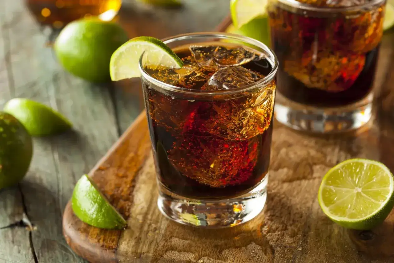 Orzeźwiający drink: bacardi z colą i limonką, podany z lodem na drewnianej desce.